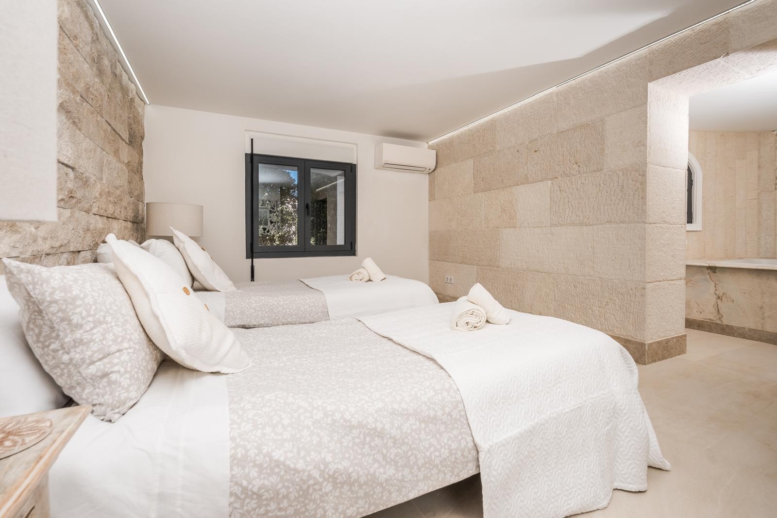 Bedroom featuring natural stone walls, recessed LED lighting, and twin beds. The space includes air conditioning and an integrated bathroom with marble details.