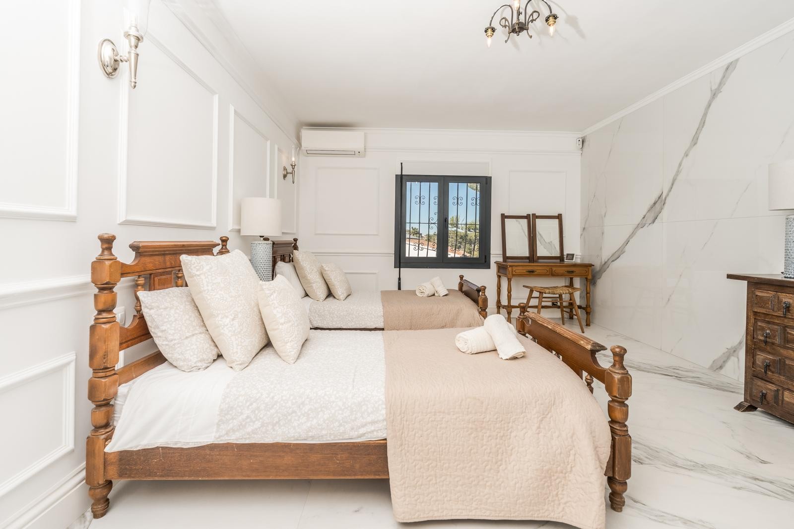 Bedroom featuring twin wooden beds, decorative wall moldings, and marble flooring. The space includes a rustic vanity, air conditioning, and a large-format stone accent wall.