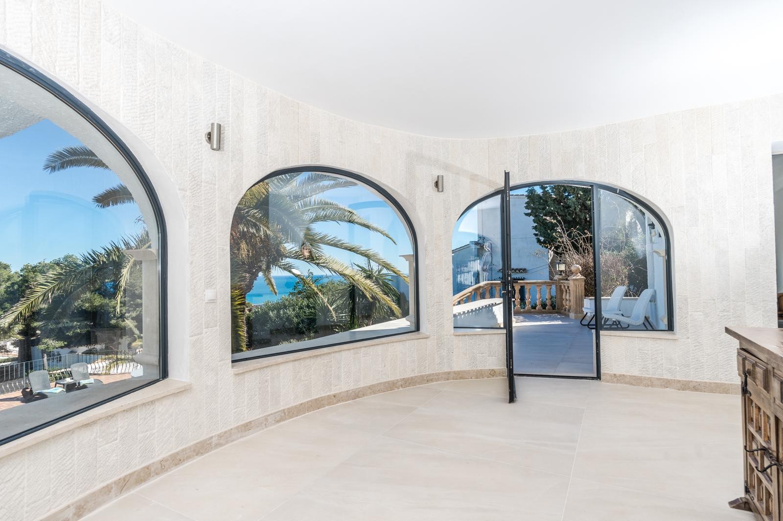Circular living area featuring textured natural stone walls and large arched windows that frame sea views and provide access to the outdoor terrace.