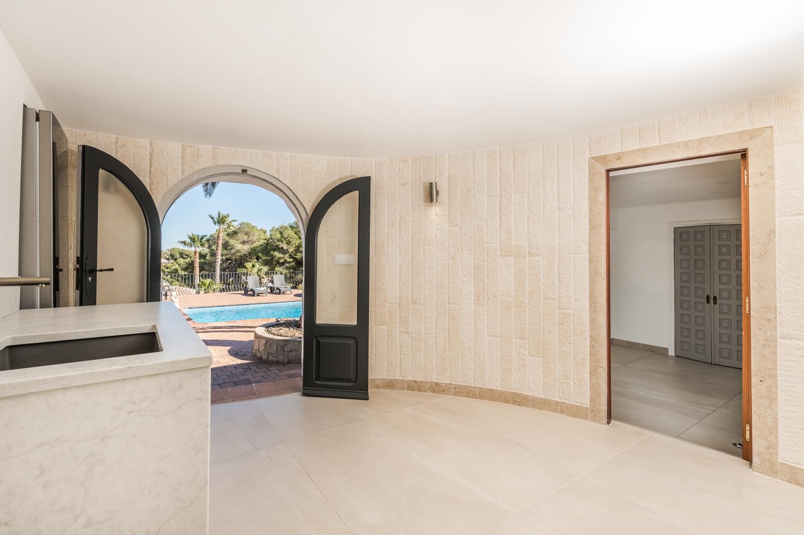Interior space featuring natural stone-clad walls and a marble counter, offering direct access to the pool terrace through a distinctive arched doorway.