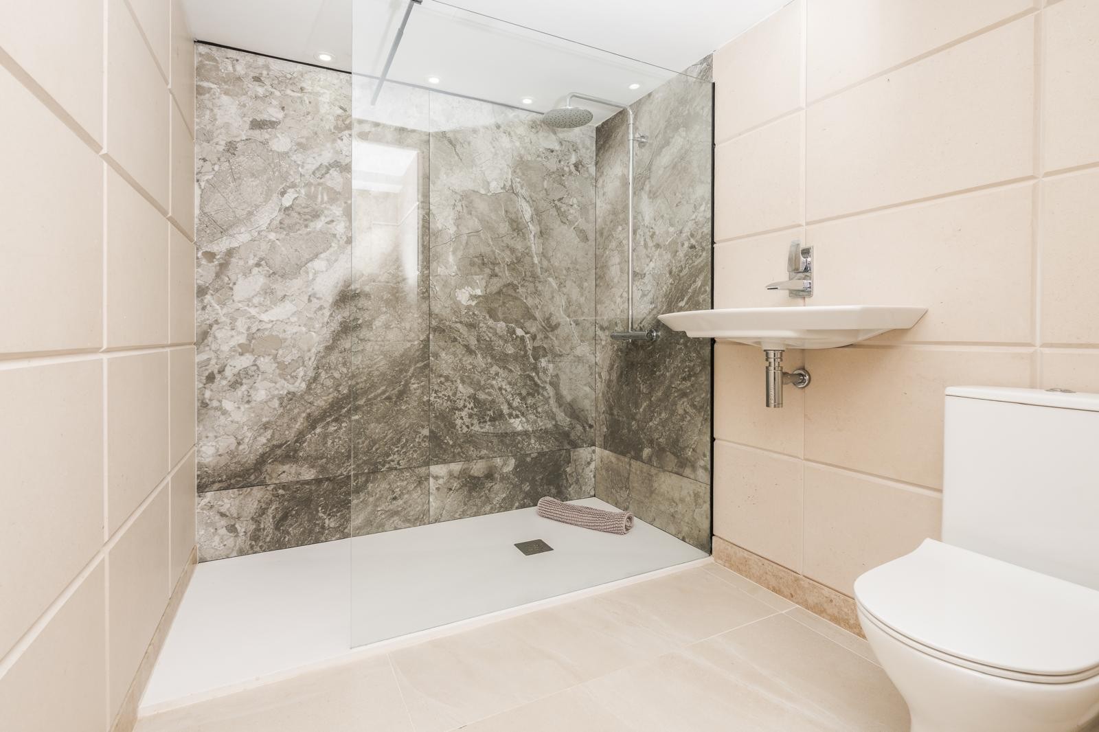 Modern bathroom featuring a walk-in shower with a glass screen and grey marble-effect wall tiles. Includes a wall-mounted sink and minimalist chrome fixtures.