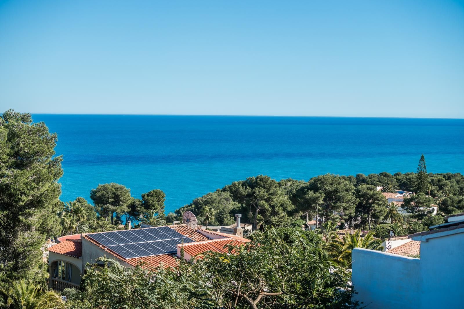 Panoramic Mediterranean Sea views from Balcón al Mar, overlooking a lush pine forest and rooftops equipped with solar panels for energy efficiency.