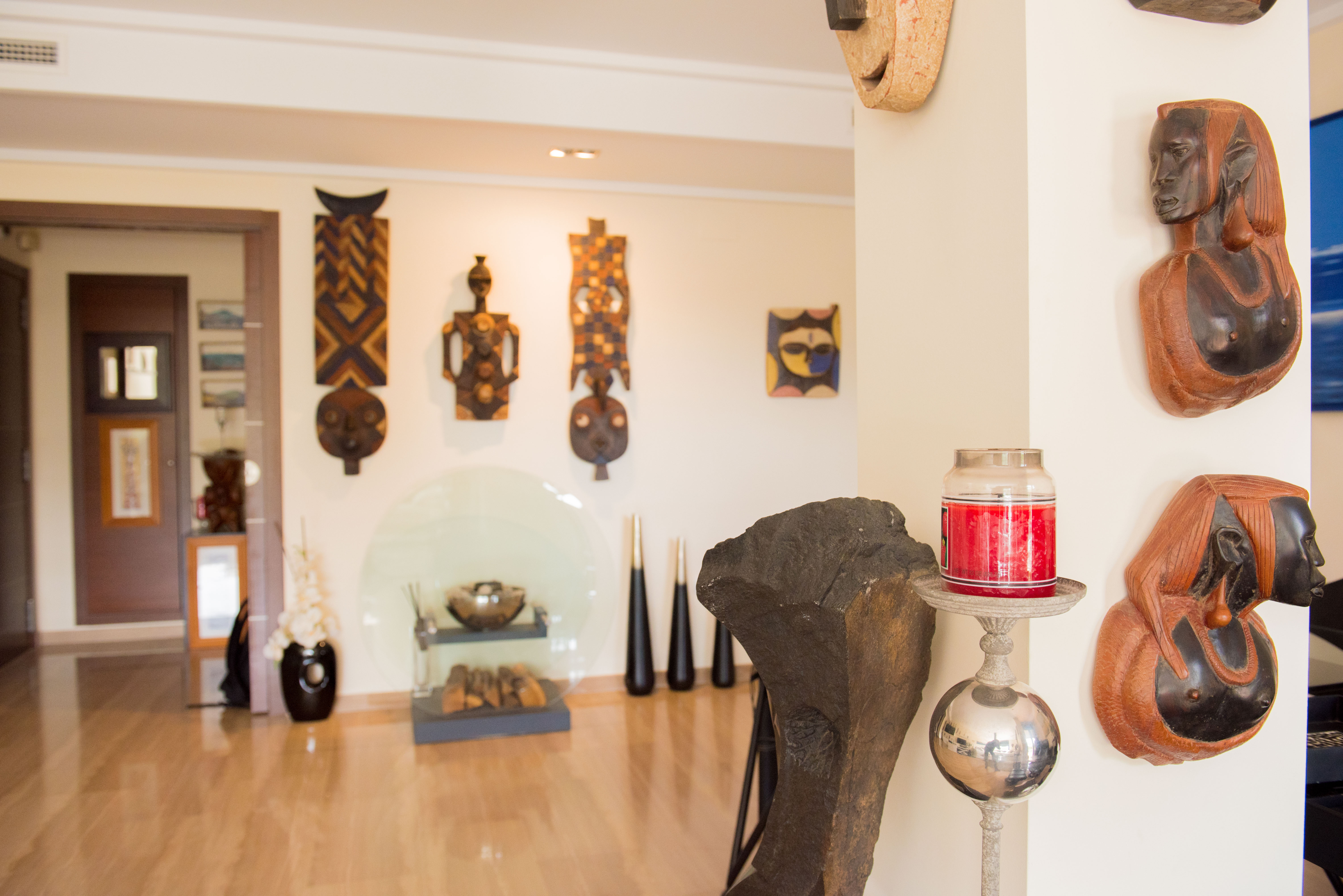 An artistic interior showcasing a curated collection of carved wooden masks and busts on light walls, complemented by a polished wooden floor and modern decorative accents.