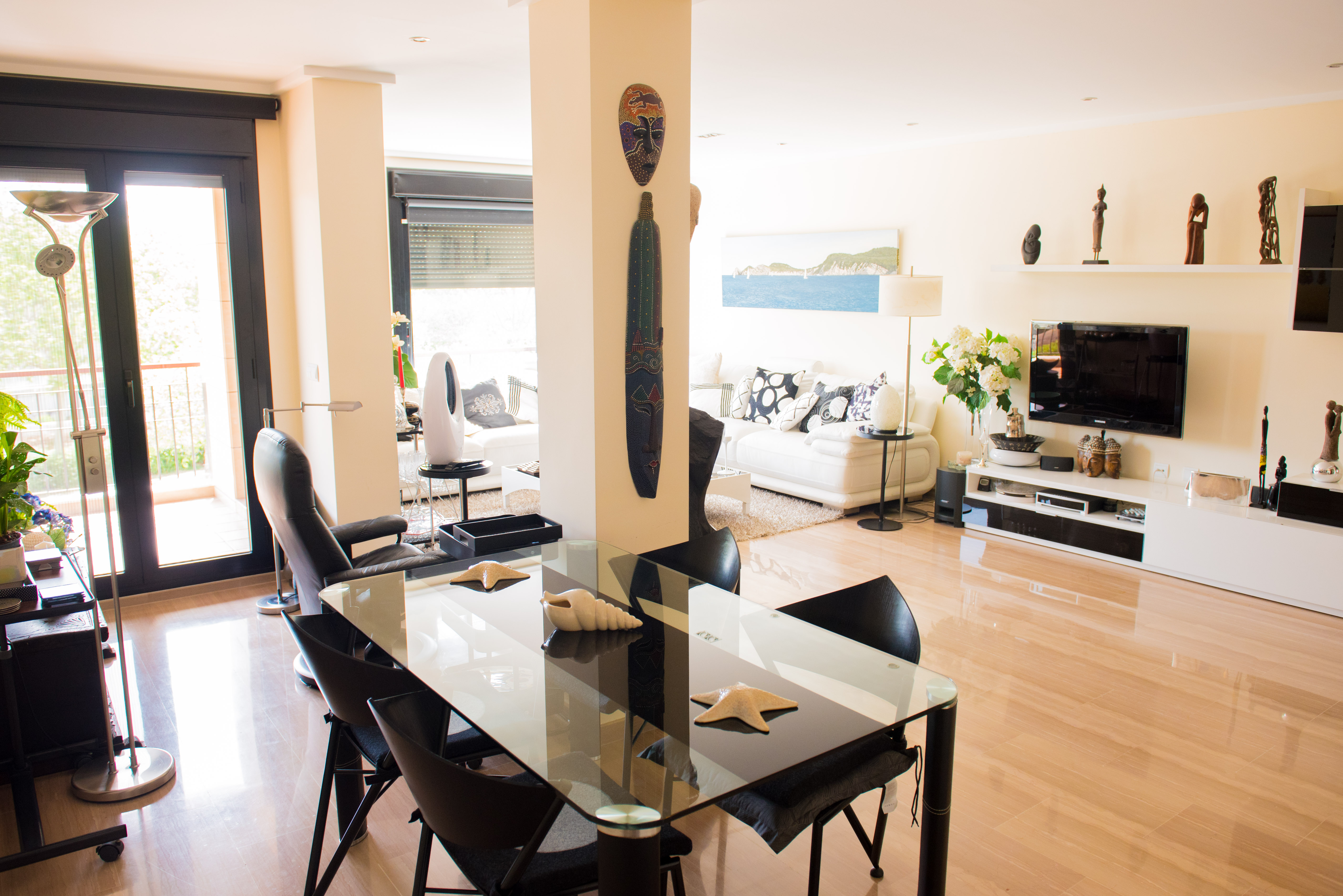 Bright open-plan living and dining area featuring polished marble floors, a glass dining table, and large glass doors leading to a private balcony.