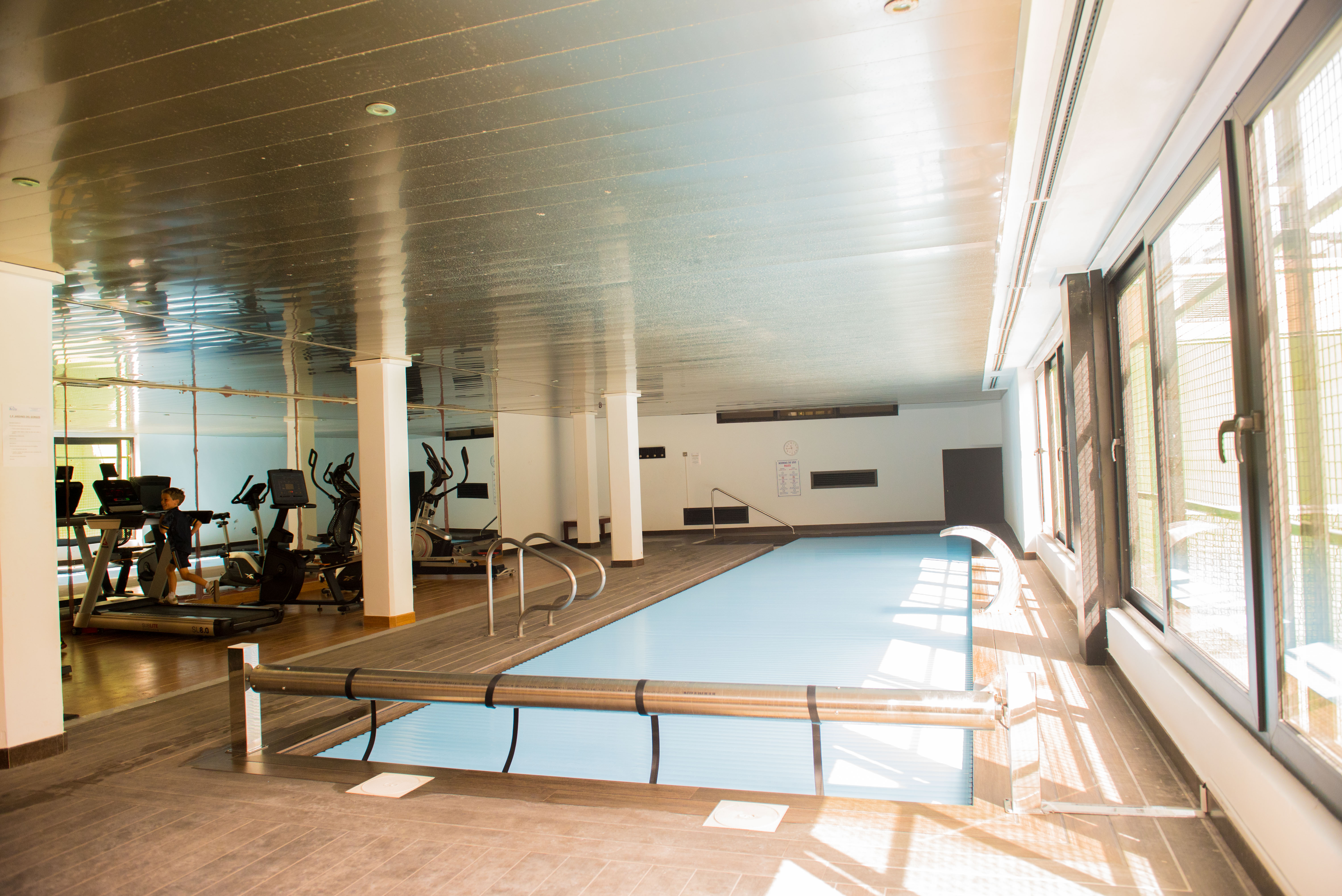 Indoor wellness area featuring a heated pool with an automatic cover and a gym equipped with treadmills and elliptical trainers.