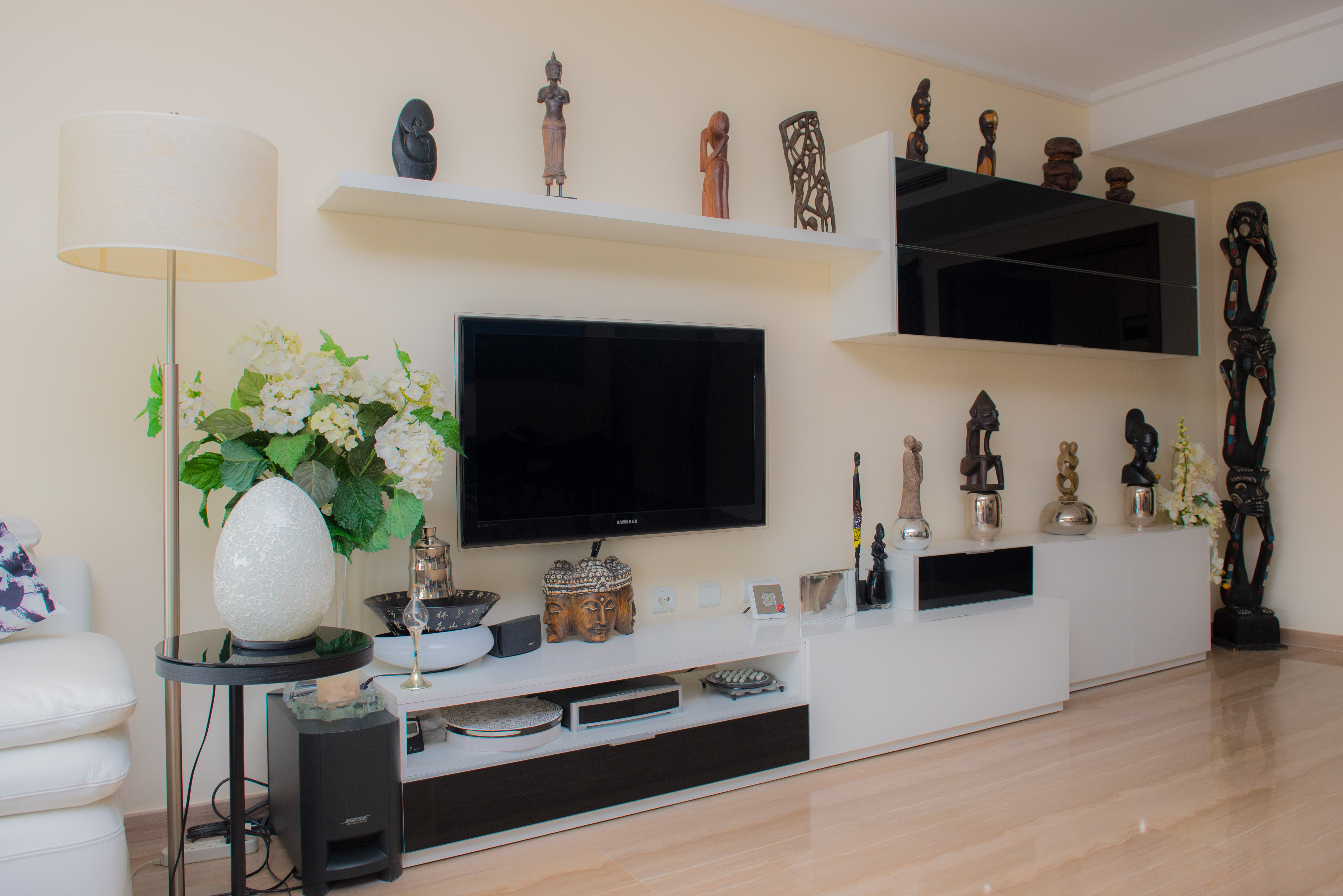 Living area featuring a modern black and white media unit, floating shelves with tribal sculptures, and polished stone flooring.
