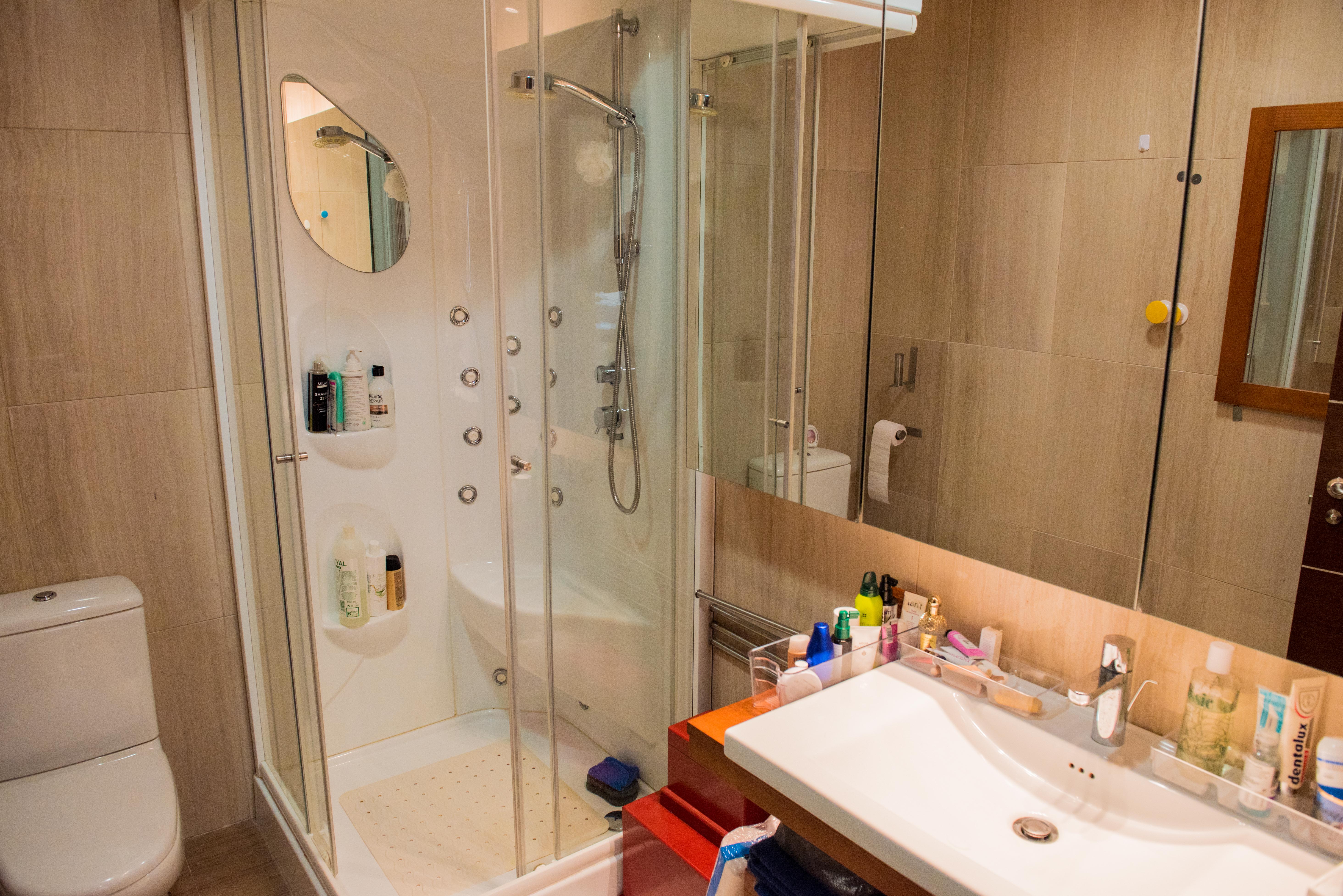 Modern bathroom featuring a hydromassage shower cabin with glass doors, a sleek white washbasin, and neutral-toned porcelain wall tiles.