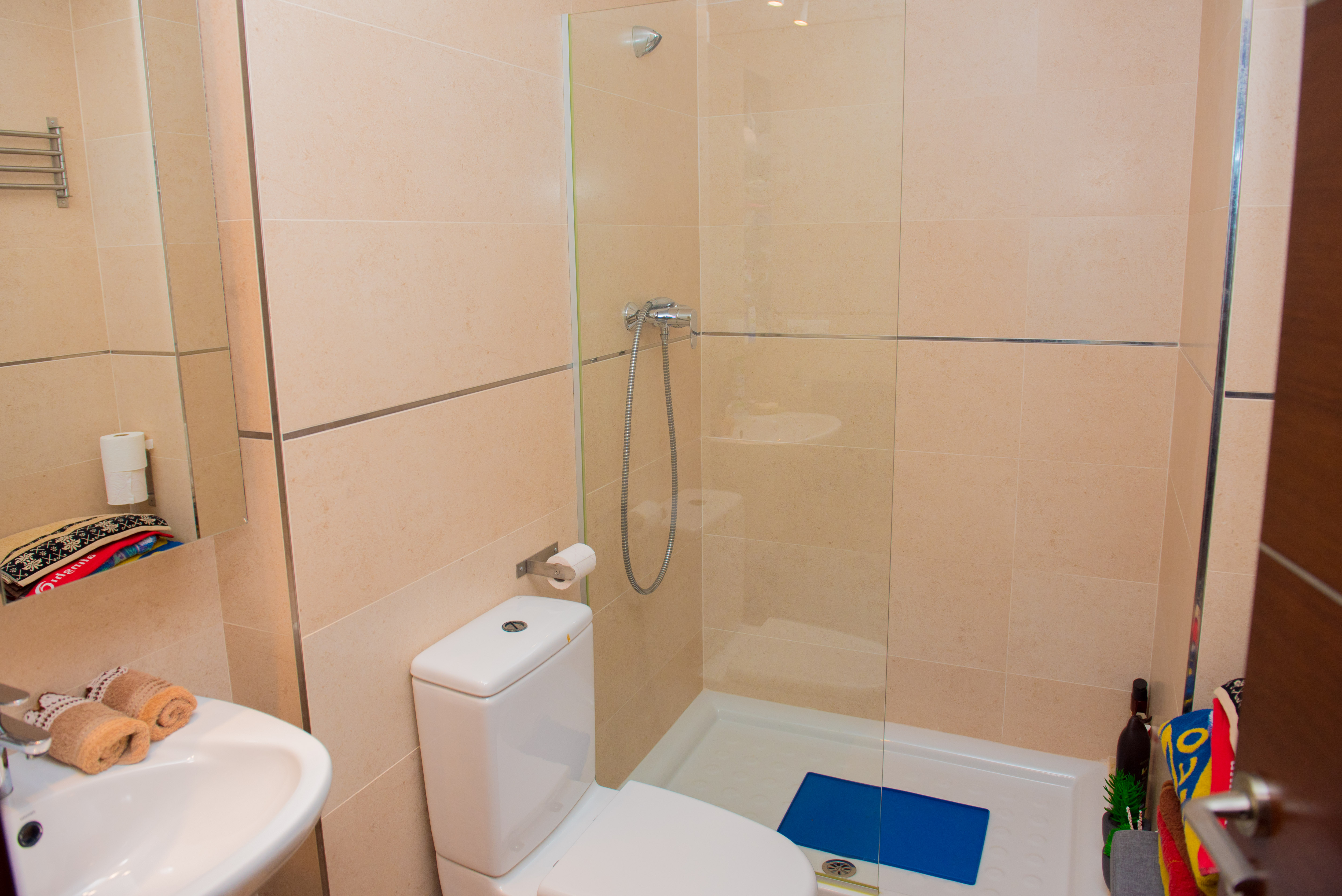 Modern bathroom featuring a walk-in shower with glass partition, white ceramic toilet, and cream-toned wall tiles with chrome accents.
