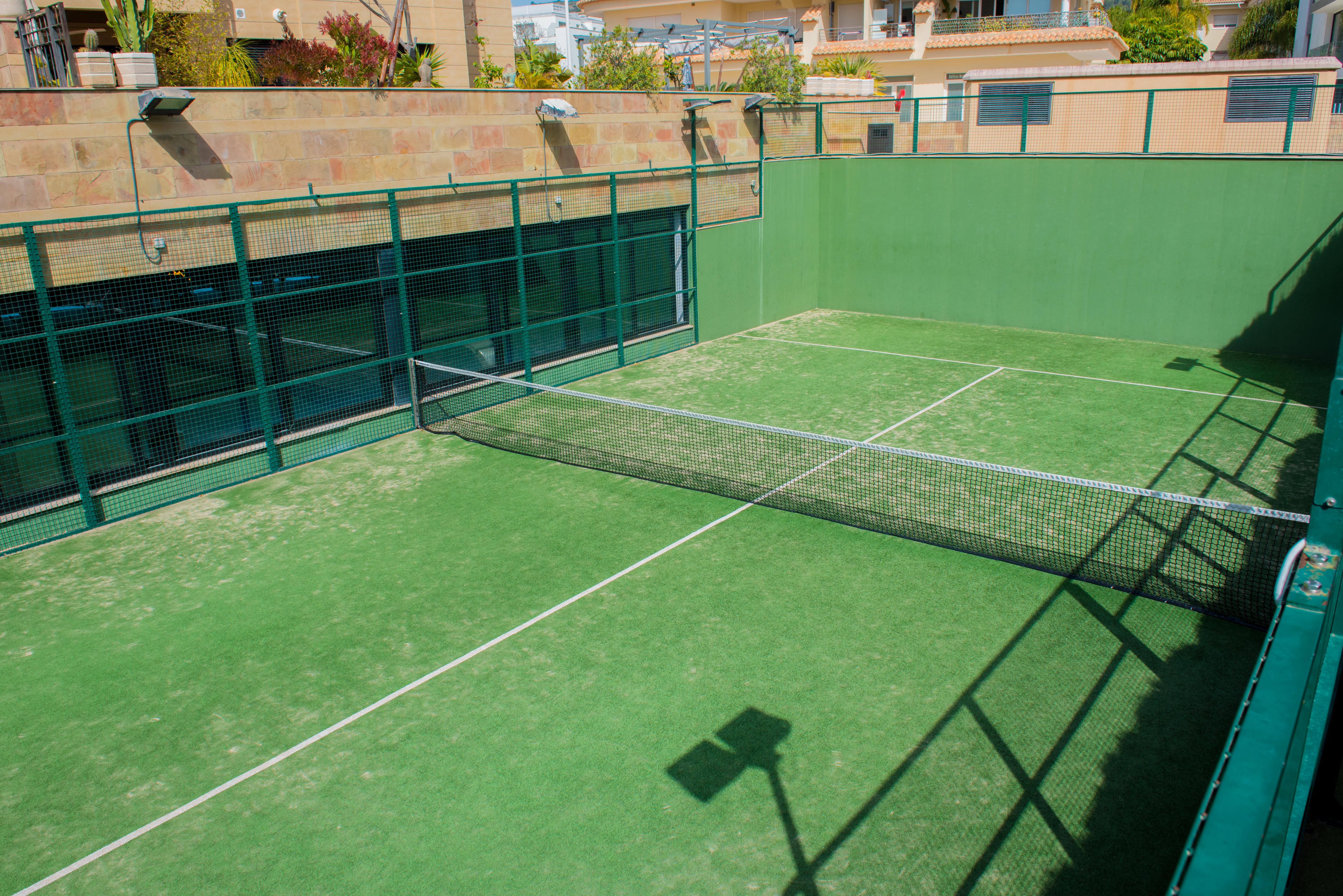 Private paddle tennis court with green artificial turf and metal fencing, located within the common areas of the residential complex in Jávea.