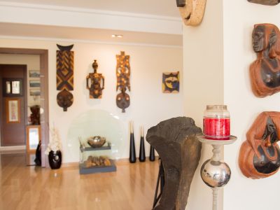 An artistic interior showcasing a curated collection of carved wooden masks and busts on light walls, complemented by a polished wooden floor and modern decorative accents.