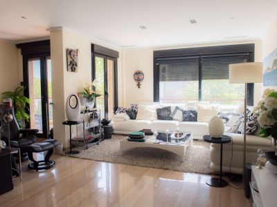 Bright living-dining area with polished marble floors and a spacious white sofa. Large glass doors with electric blinds offer outdoor access and ample natural light.