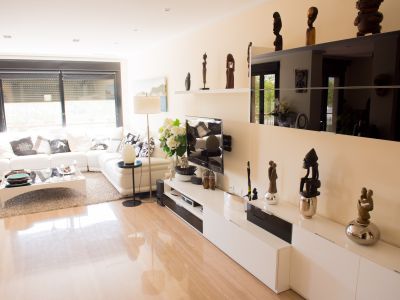 Bright living room featuring a white sectional sofa, polished light-toned tile flooring, and a modern media console. Natural light enters through the window with roller blinds.