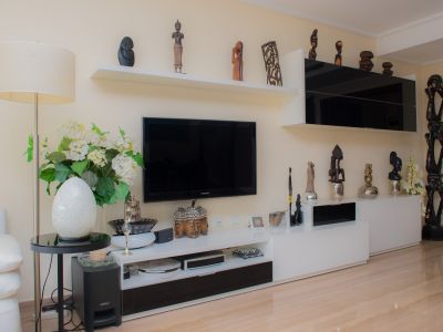 Living room featuring a modern black and white TV unit, floating shelves displaying diverse sculptures, and light polished porcelain floor. A floor lamp and decorative accents complete the space.