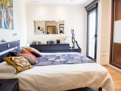 Master bedroom featuring a double bed with a dark headboard and integrated reading lamps, direct terrace access, and a built-in wardrobe with wood and frosted glass doors.