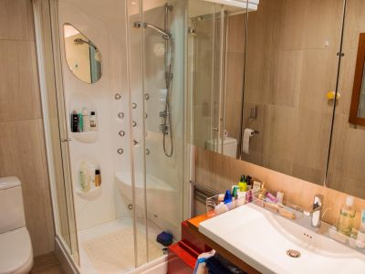 Modern bathroom featuring a glass-enclosed shower cabin with multiple hydro-massage jets and an integrated vanity sink. Beige tiled walls complete the space.