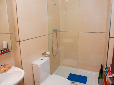 Modern bathroom featuring light beige tiled walls with metallic accents. Includes a white toilet, sink with chrome faucet, and a glass-enclosed shower with a white tray.