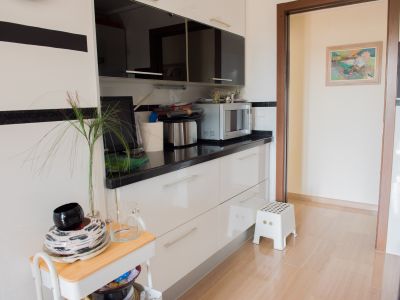 Modern kitchen featuring sleek white base cabinets, black countertops, and reflective black upper units. Equipped with a microwave, it opens to an adjacent room with light tiled flooring.
