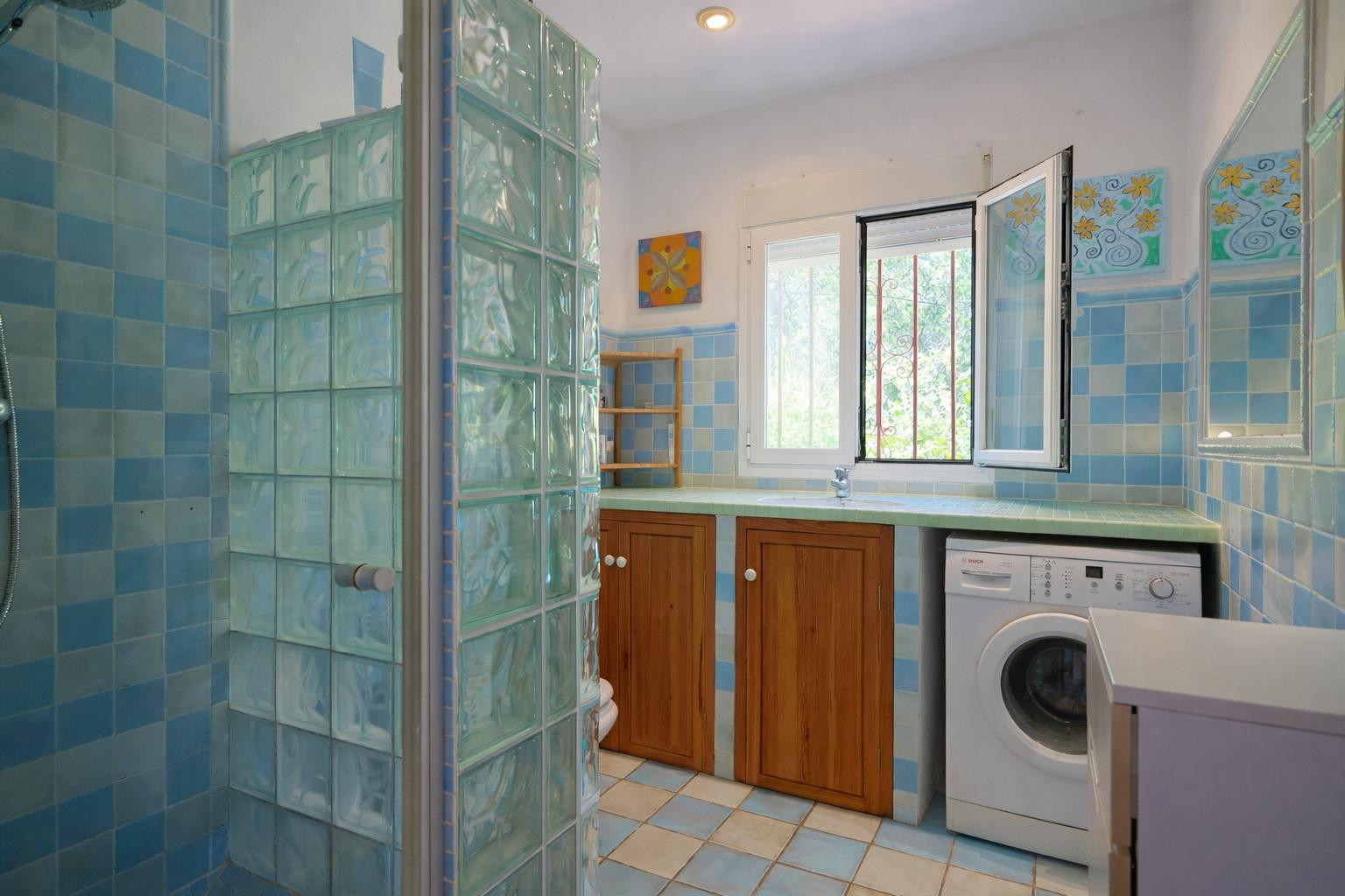 Functional bathroom and laundry area featuring blue checkered tiling, a glass block shower screen, wooden cabinetry, and an integrated washing machine.