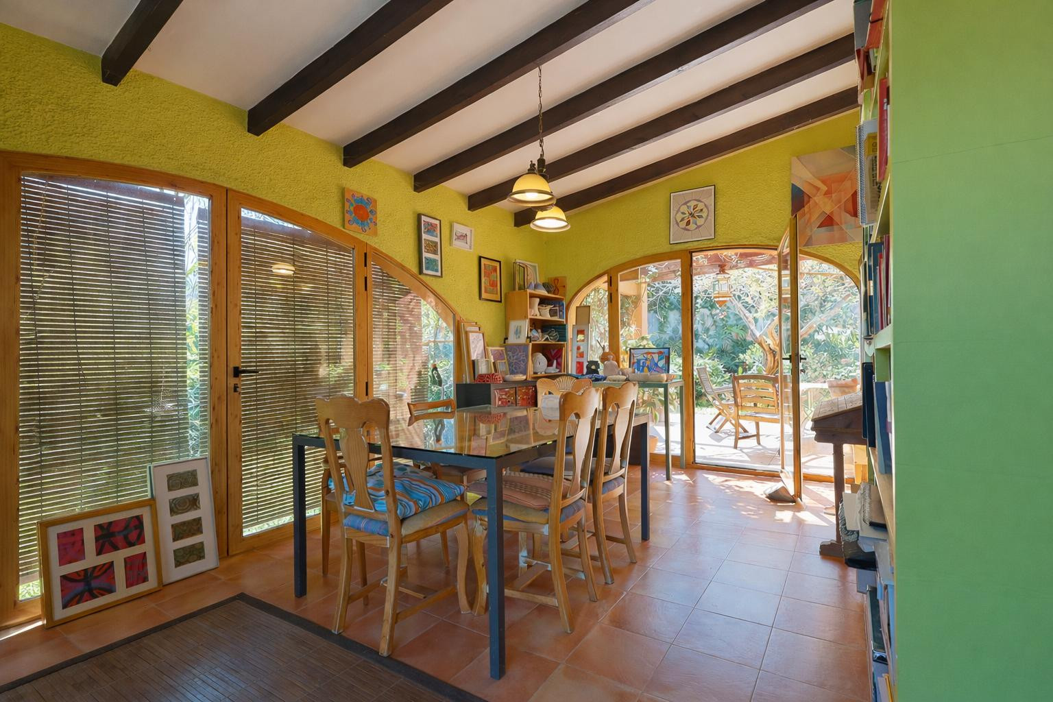 Glazed naya featuring exposed wooden beams, terracotta flooring, and arched glass doors that provide seamless access to the garden.