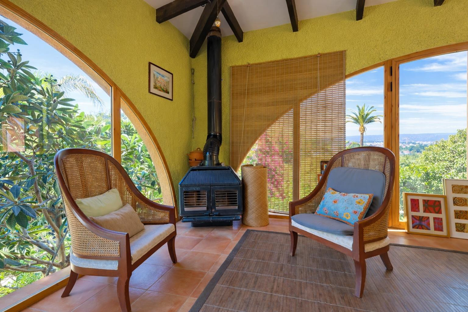 Glazed sunroom featuring exposed wooden beams, a pellet stove, and arched windows providing natural light and views of the surrounding landscape.