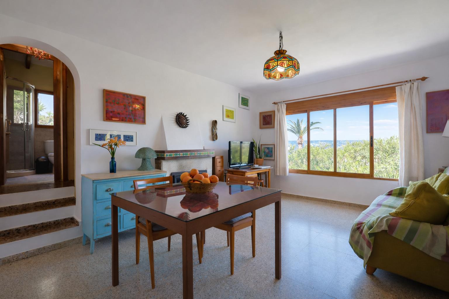 Living and dining area featuring a fireplace, terrazzo flooring, and sea views. An arched doorway leads to an elevated bathroom equipped with a walk-in shower.