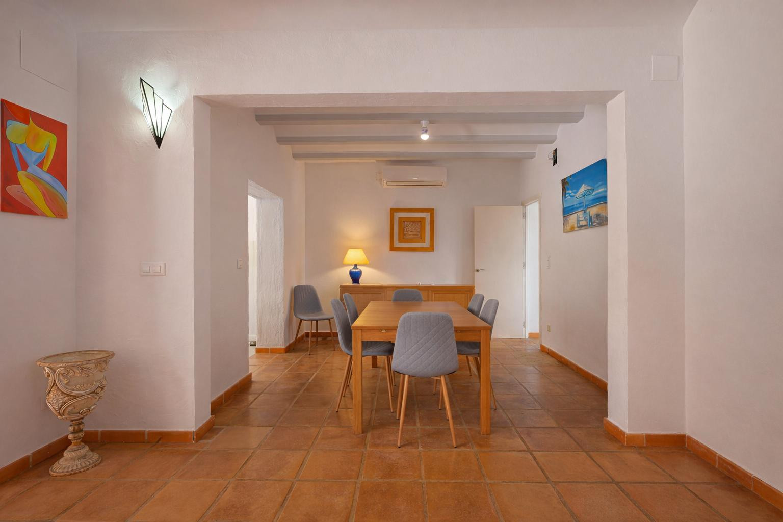 Dining area featuring a wooden table with grey upholstered chairs, terracotta tile flooring, and exposed ceiling beams. Equipped with split-system air conditioning.