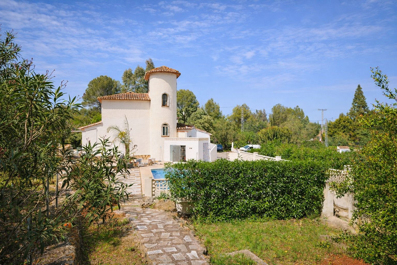 Exterior view of the villa featuring a circular tower, terracotta tiled roof, and Mediterranean garden with stone paths and a private pool.