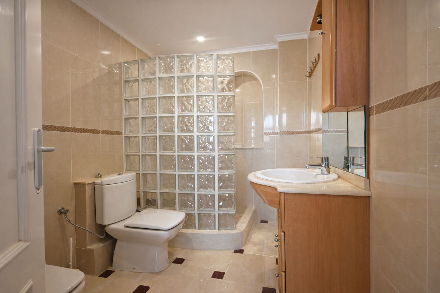 Full bathroom featuring cream-toned wall tiles, a walk-in shower with a glass block partition, and a wooden vanity unit with an integrated mirror.