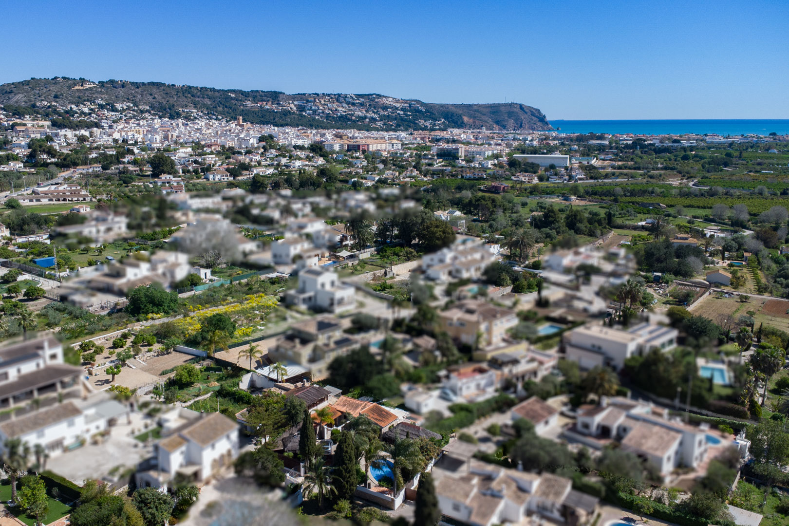 Aerial view of the residential area in Jávea, highlighting the proximity to the town center, the Mediterranean coast, and the surrounding hills.