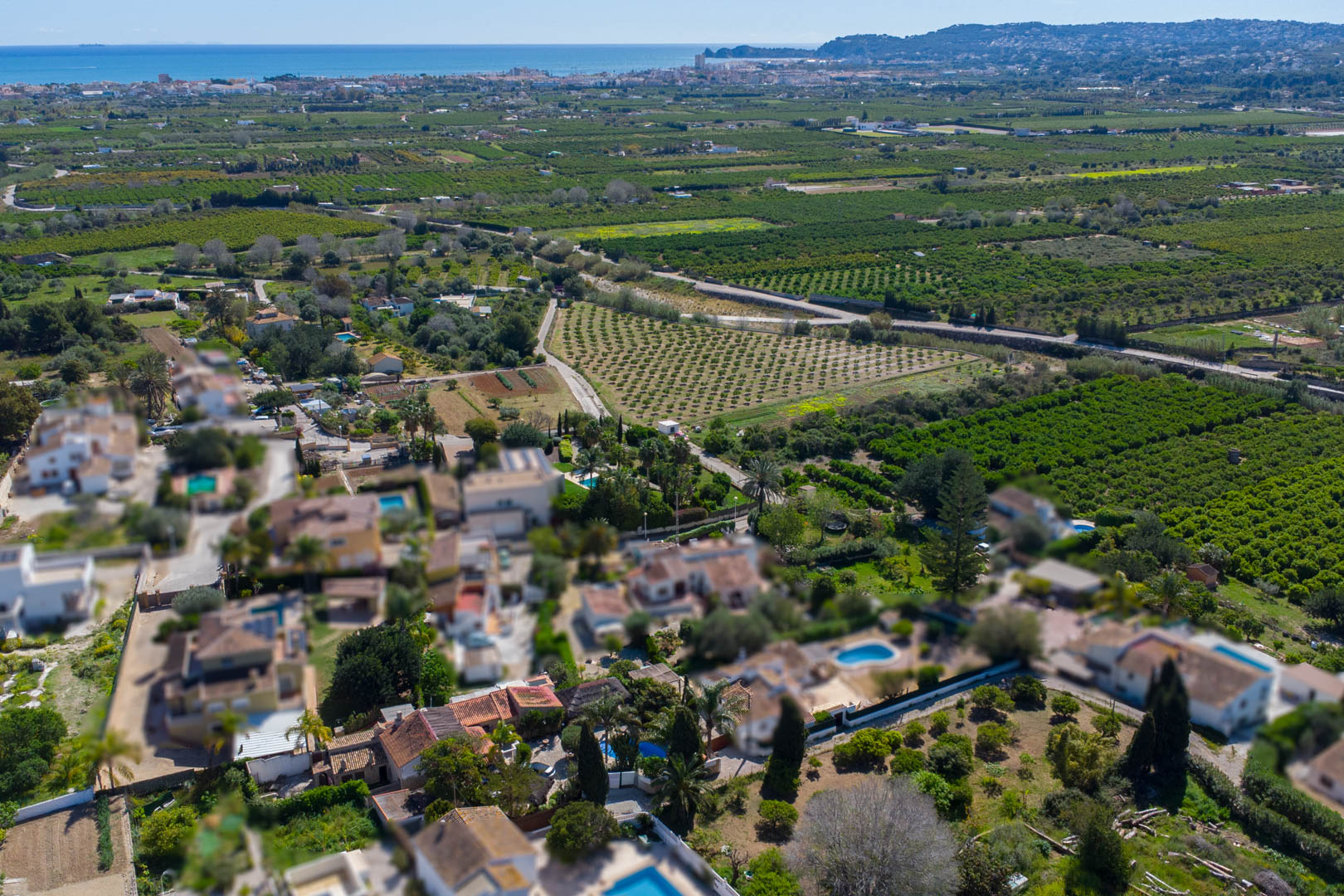 Aerial view showcasing the property's location amidst lush orchards, with the Mediterranean coastline and Jávea bay visible on the horizon.