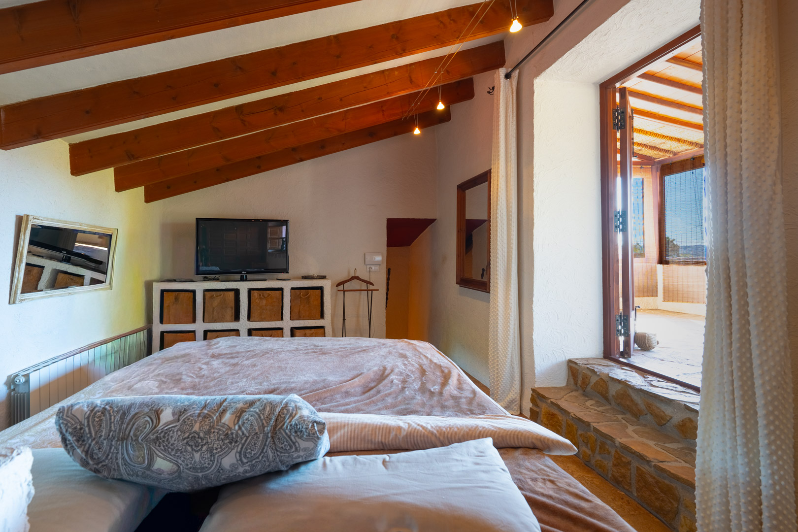 Bedroom featuring exposed wooden beams and stone steps leading to a bright, glazed naya with rustic architectural details.