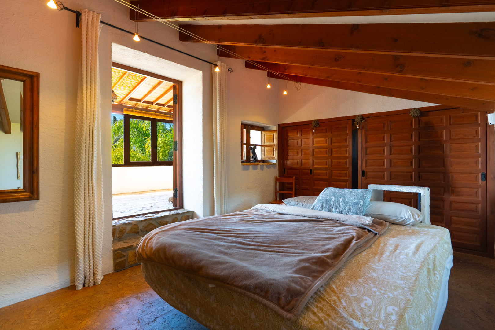 Bedroom featuring sloped wooden beam ceilings, integrated wardrobes, and a large opening leading to a private terrace with garden views.