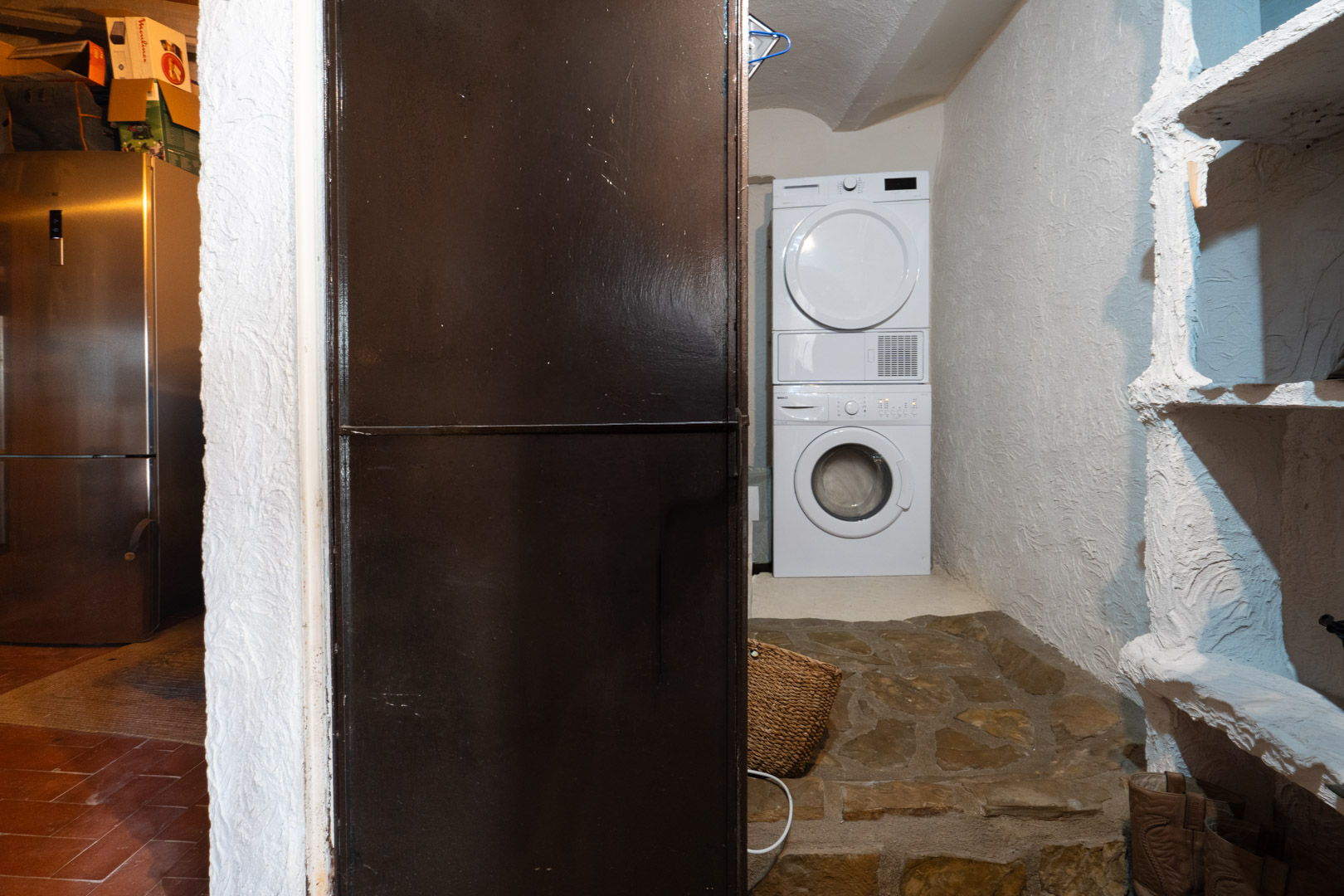Functional laundry area featuring a stacked washer and dryer, textured plaster walls, and rustic natural stone flooring.