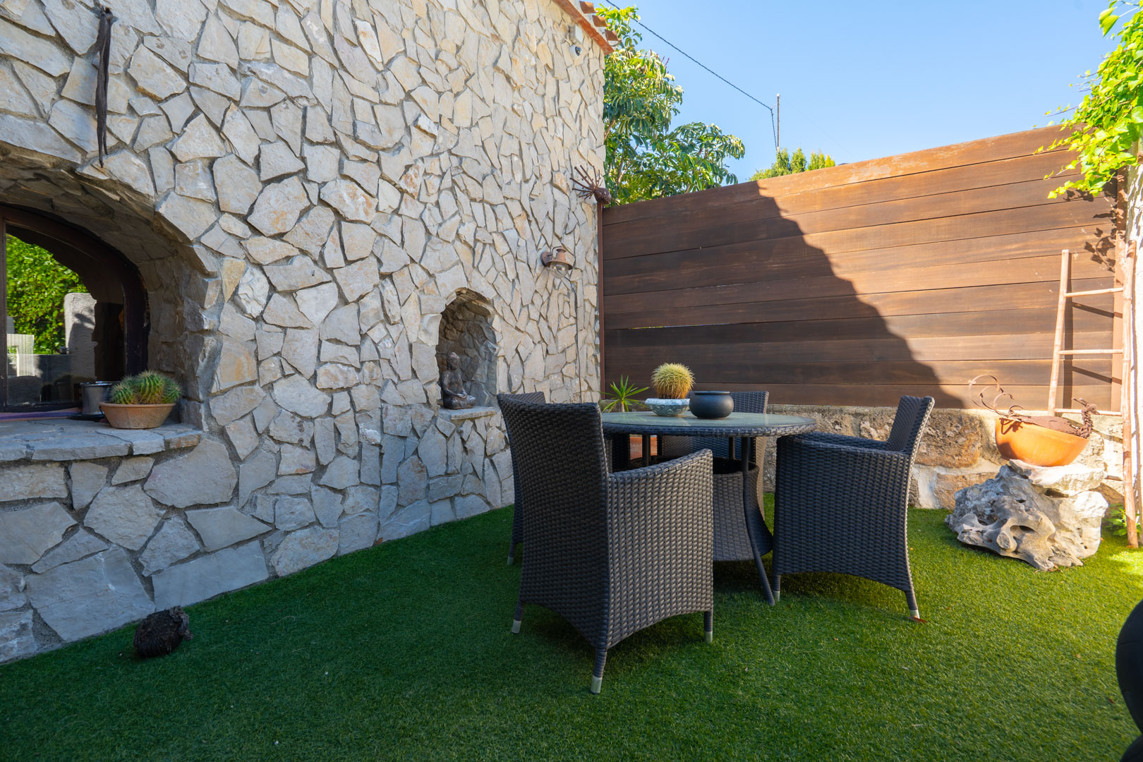 Outdoor patio featuring a natural stone facade with integrated niches, a dark wicker dining set, and artificial turf flooring.