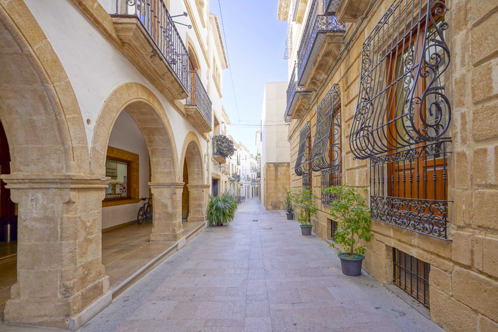 Pedestrian street in the historic center featuring traditional stone facades, Tosca stone arches, and ornate wrought iron window grilles.