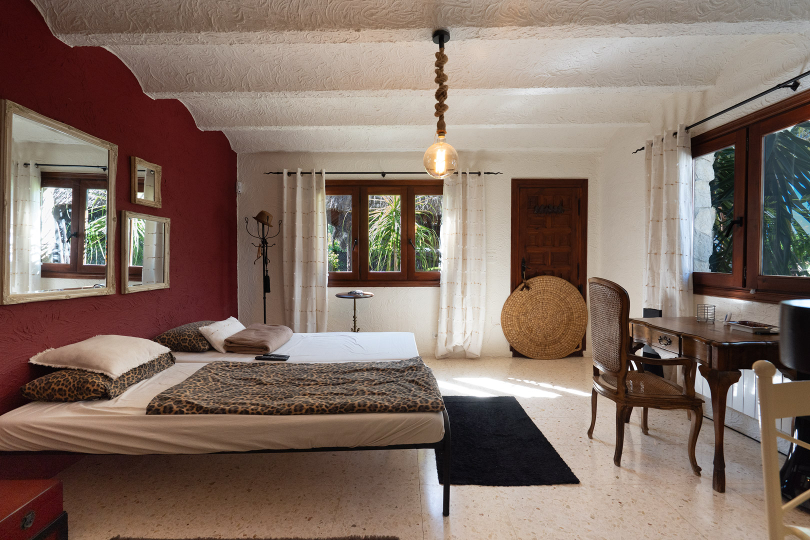 Rustic bedroom featuring a burgundy accent wall, vintage wooden desk, and textured plaster ceilings. Includes terrazzo flooring and a unique rope-suspended light fixture.