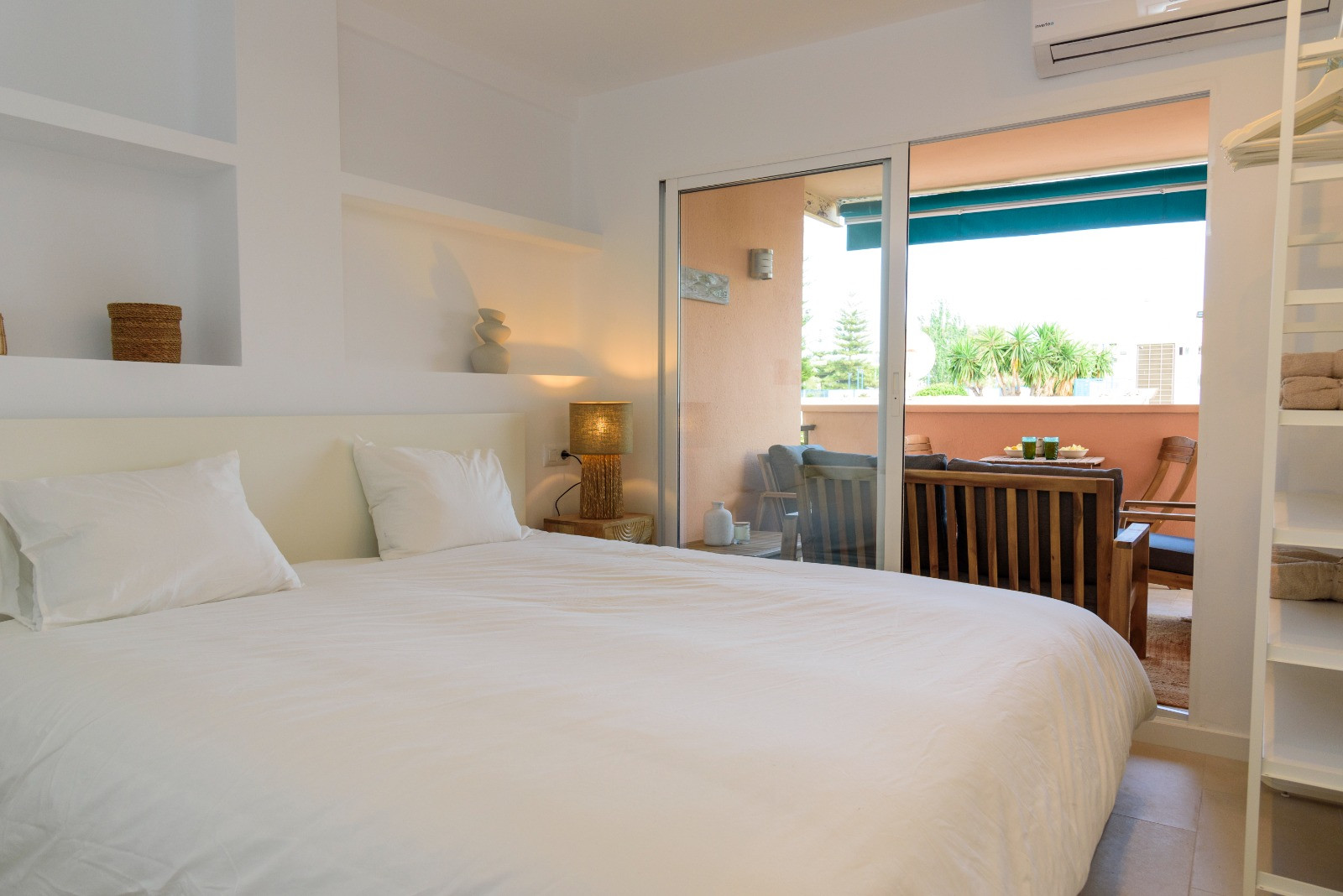 Bedroom featuring recessed wall shelving and sliding glass doors that open onto a furnished terrace, maximizing natural light and outdoor connectivity.
