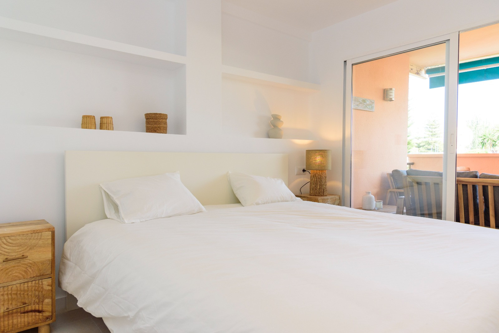 Bright bedroom featuring built-in wall shelving, wooden nightstands, and direct access to a private terrace through large sliding glass doors.
