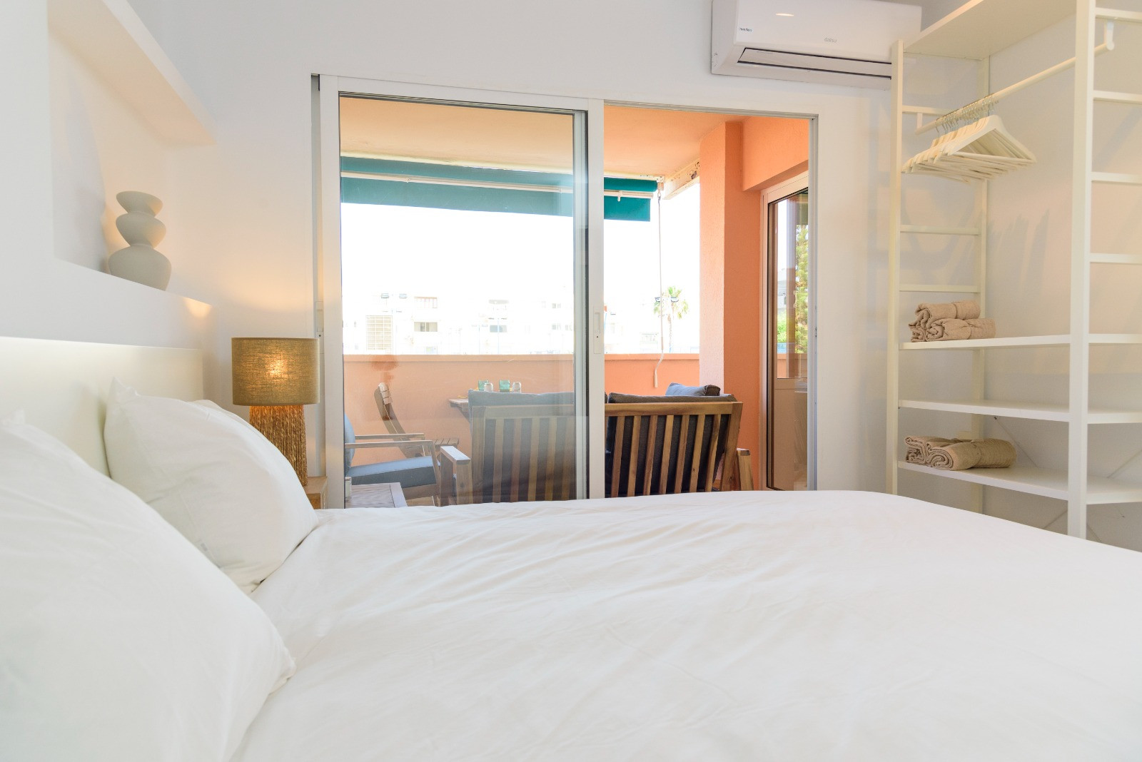 Bright bedroom featuring direct access to a furnished terrace, a minimalist open wardrobe system, and split-unit air conditioning.