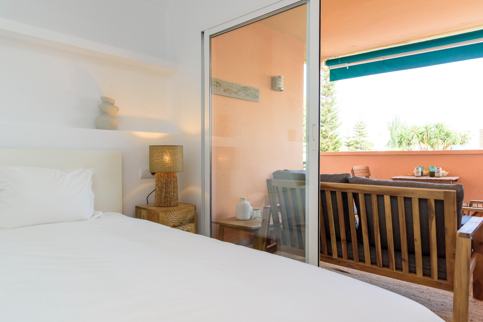 Bright bedroom featuring direct access to a private terrace with wooden lounge furniture. The space offers natural light and a minimalist design with neutral tones.