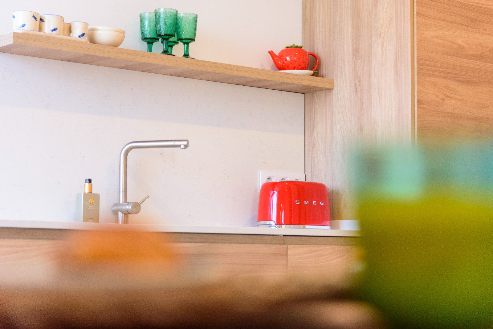 Kitchen detail featuring a white stone countertop, minimalist faucet, and wooden shelving. Accented with designer appliances and natural finishes.