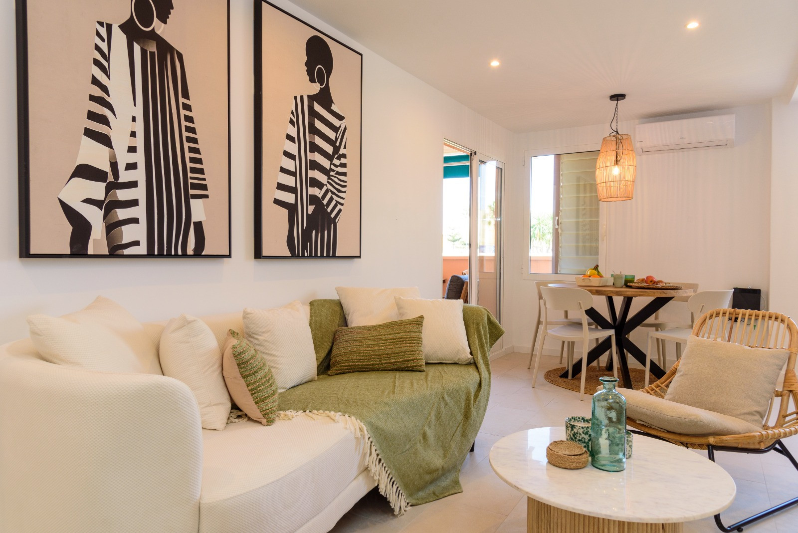 Open-plan living and dining area featuring contemporary art, a marble coffee table, and a rattan armchair. The space includes a wooden dining set and seamless access to the terrace.
