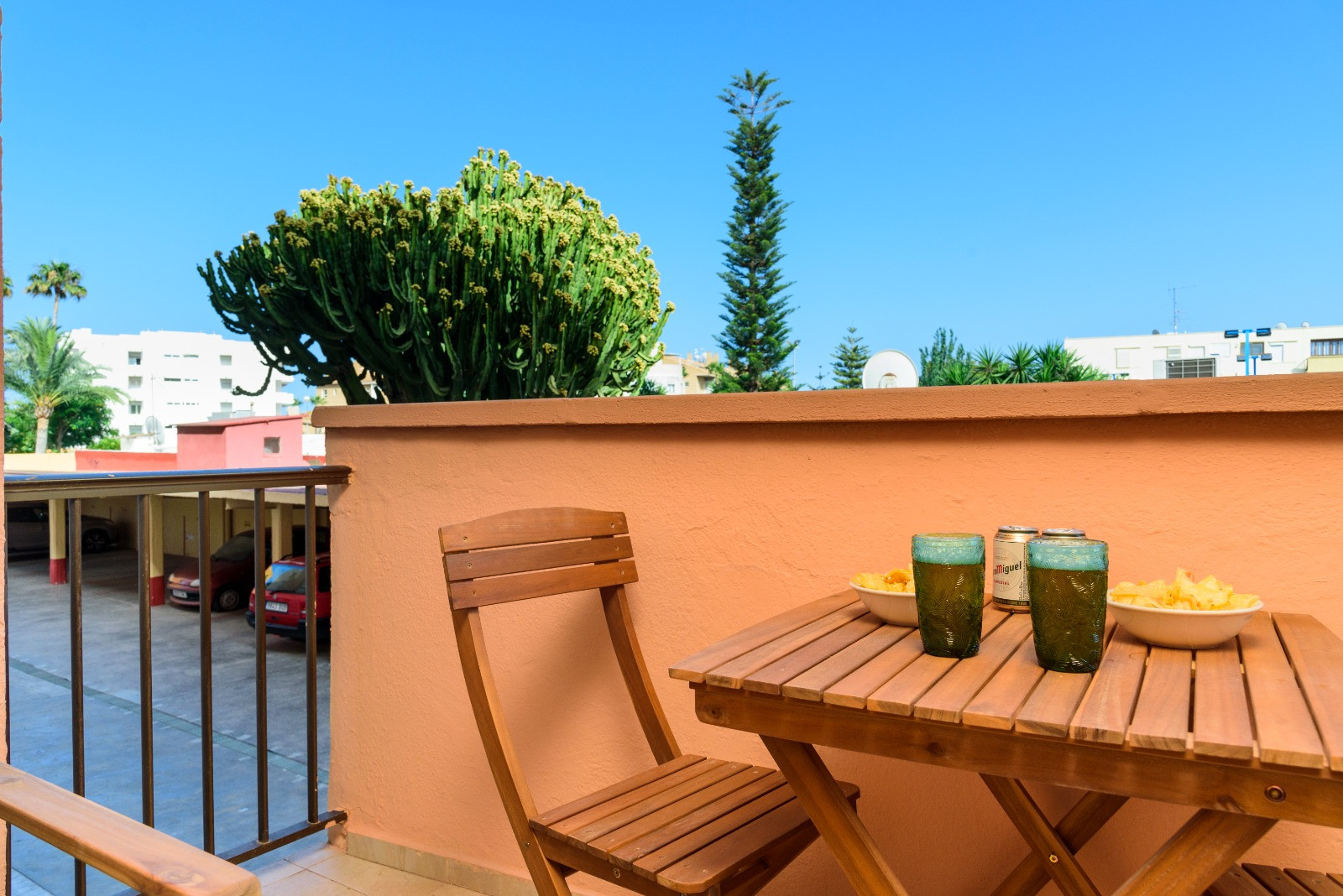 Private terrace featuring a wooden dining set, perfect for outdoor snacks. The space overlooks a landscaped area with mature cacti and palm trees under a clear sky.