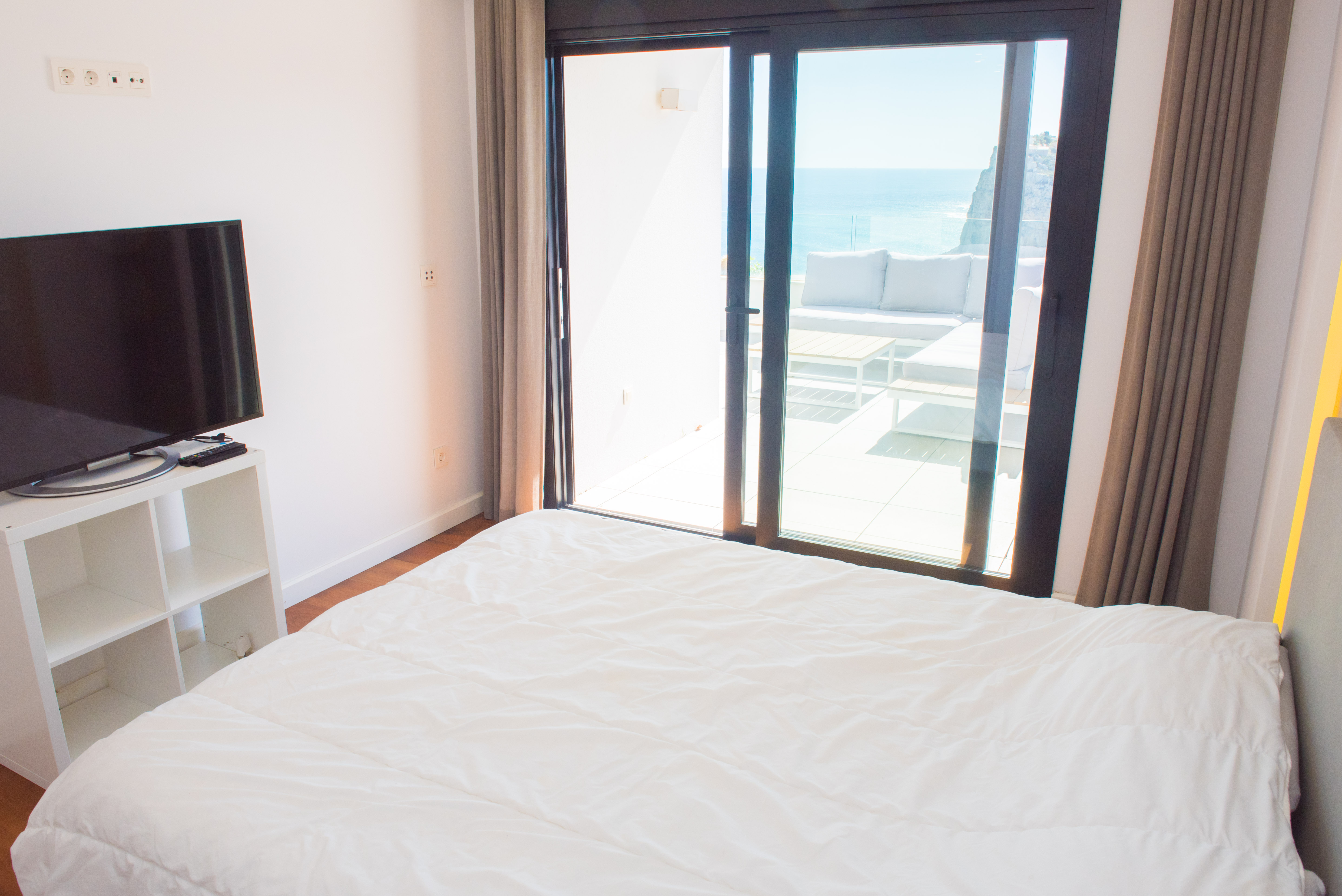 Bright bedroom featuring direct access to a private terrace with lounge furniture and expansive views of the Mediterranean Sea and surrounding cliffs.