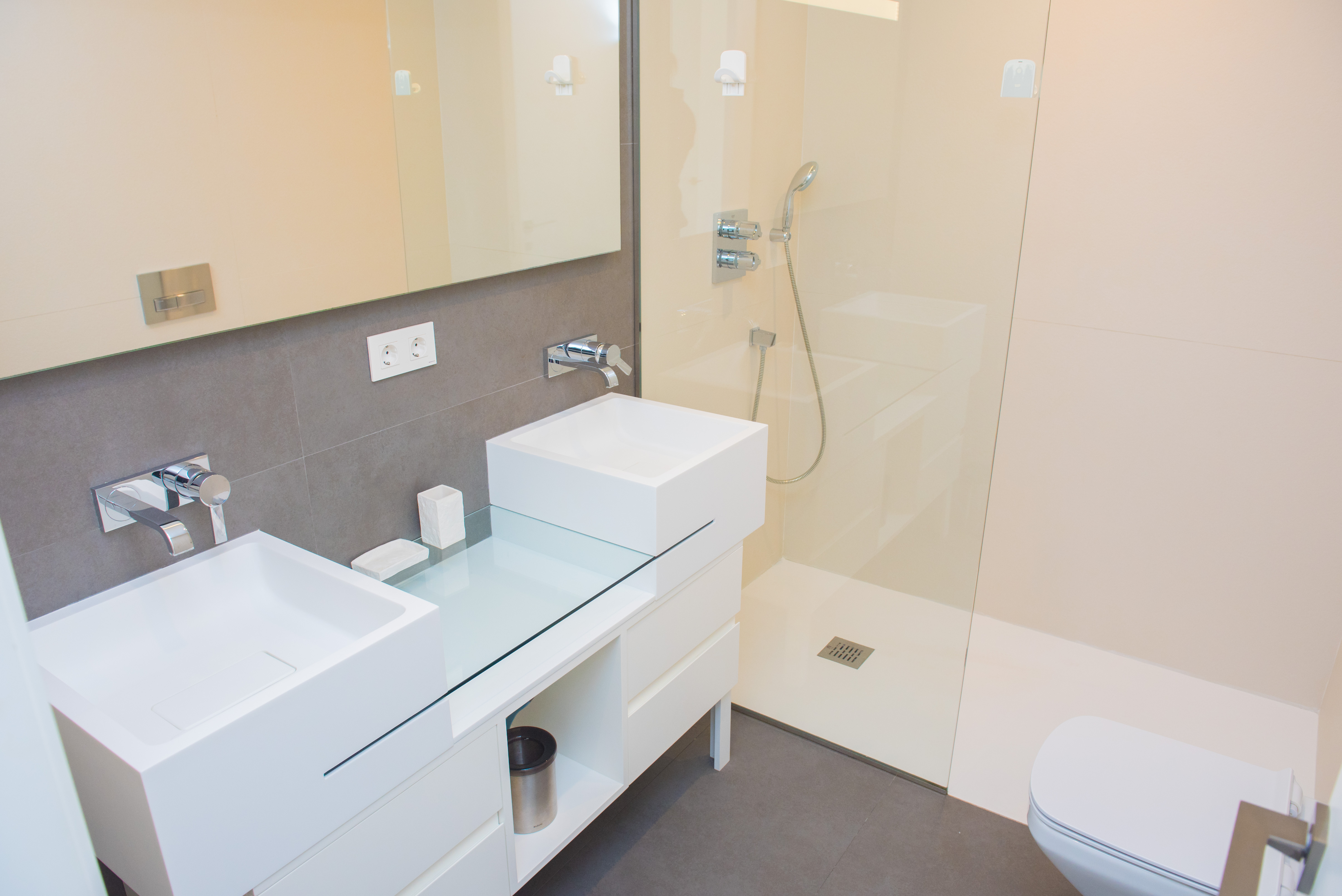Contemporary bathroom featuring a double vanity with square sinks, wall-mounted faucets, and a walk-in shower with a glass screen and integrated LED mirror.