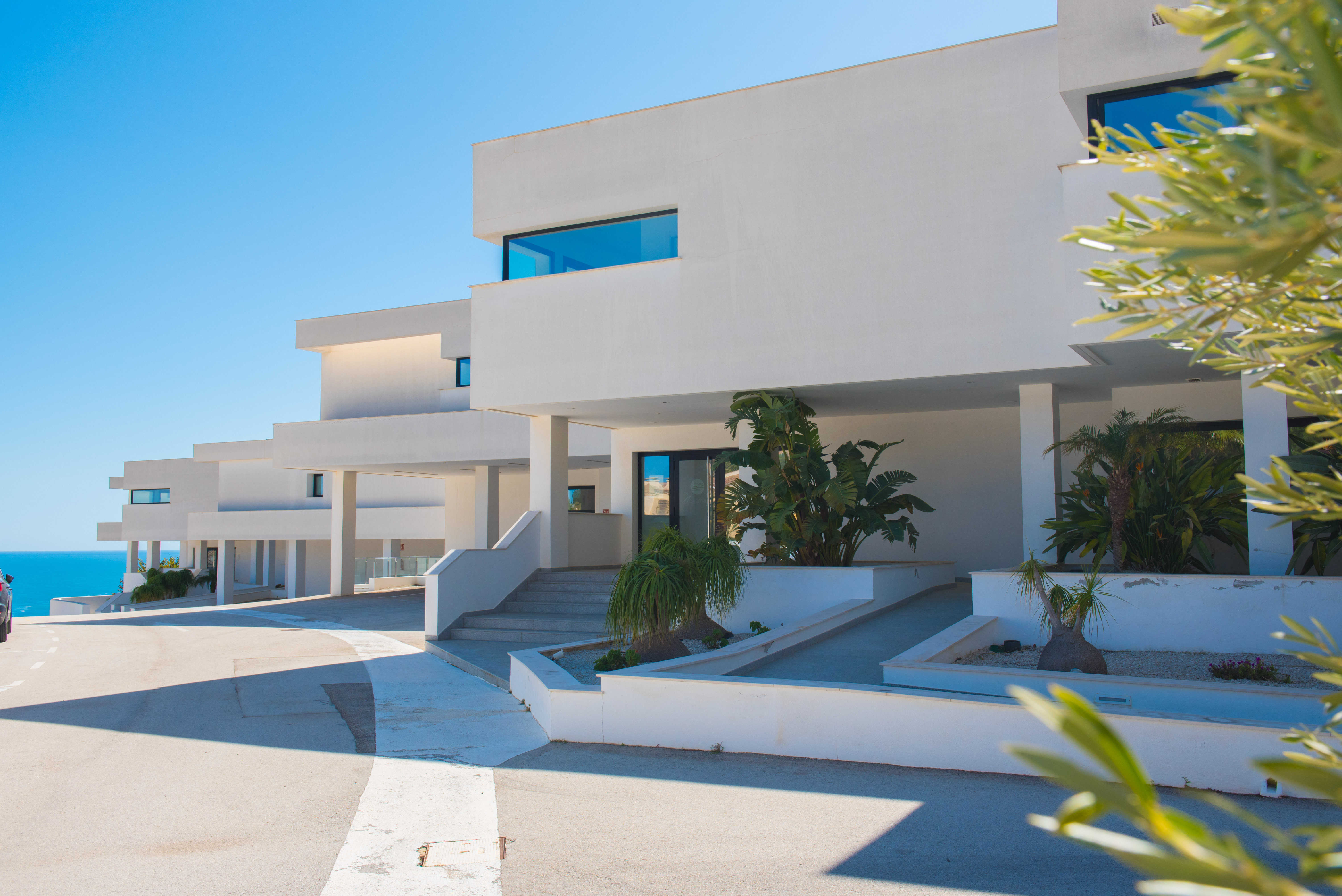 Minimalist pure white facade featuring stepped entrances and ramps, integrated planters with tropical greenery, and clean architectural lines.