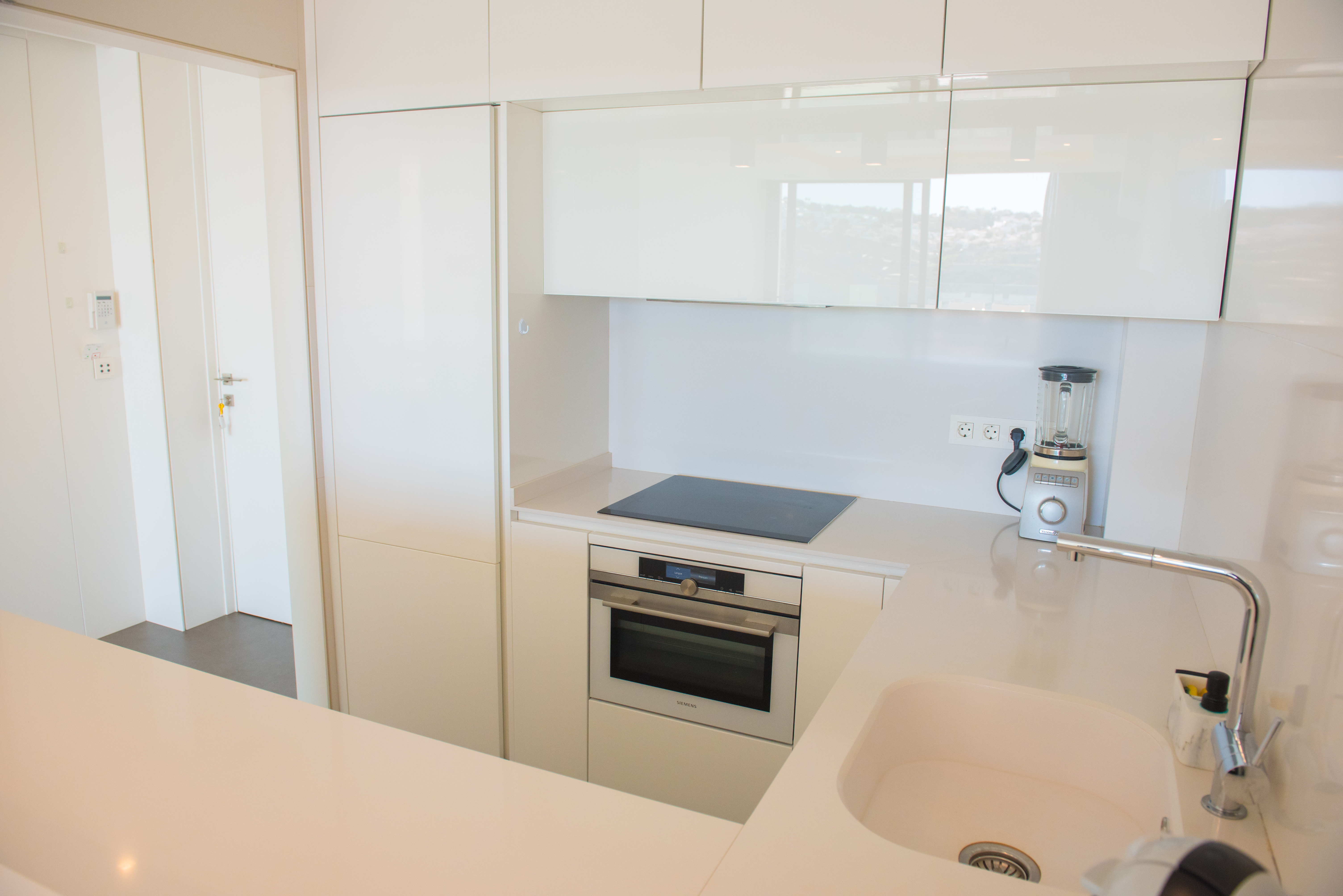 Modern kitchen featuring white glossy cabinetry, a Siemens integrated oven, induction cooktop, and a white quartz countertop with an undermount sink.