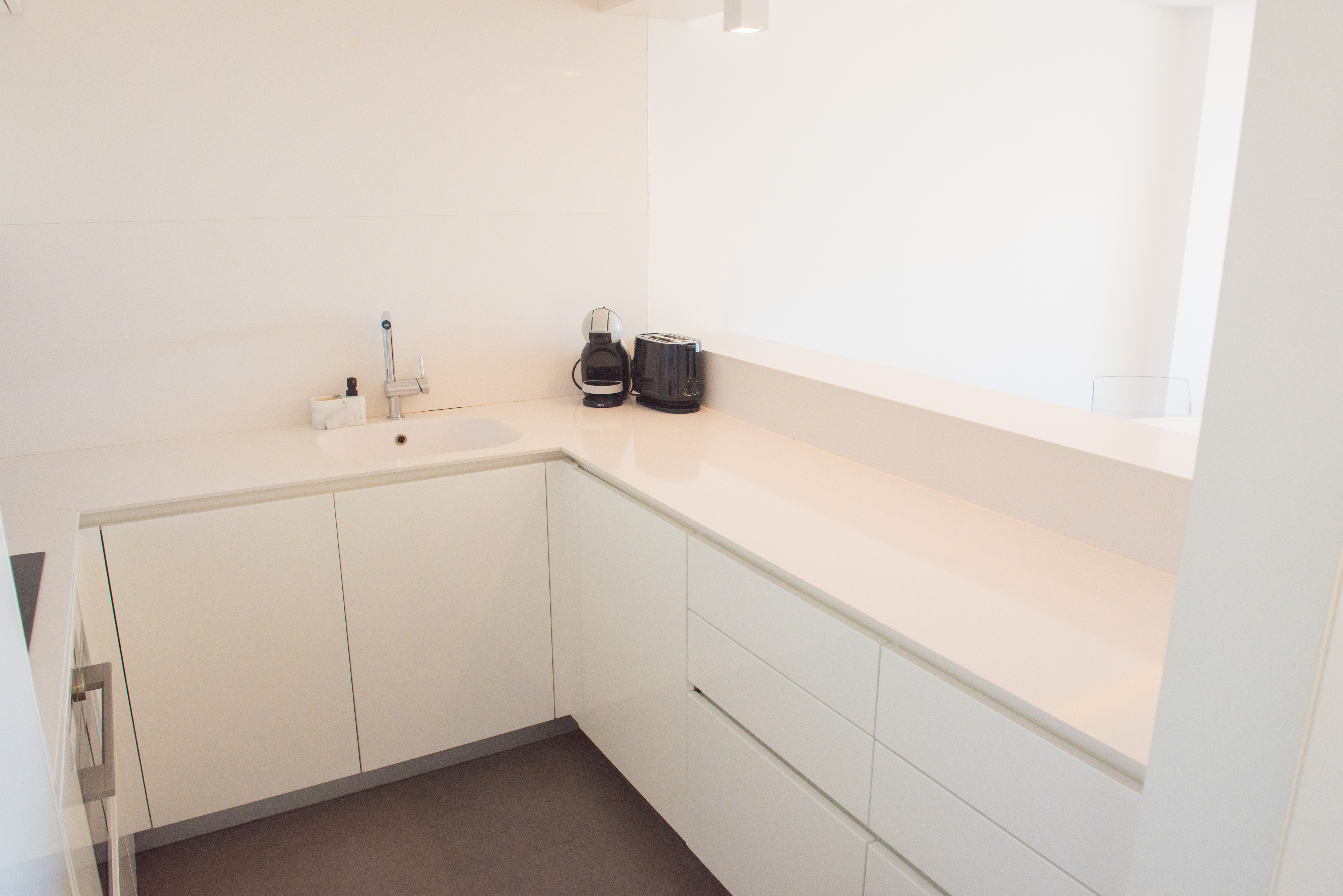 Modern minimalist kitchen in glossy white featuring a quartz countertop, integrated sink, and dark tiled flooring for a clean aesthetic.