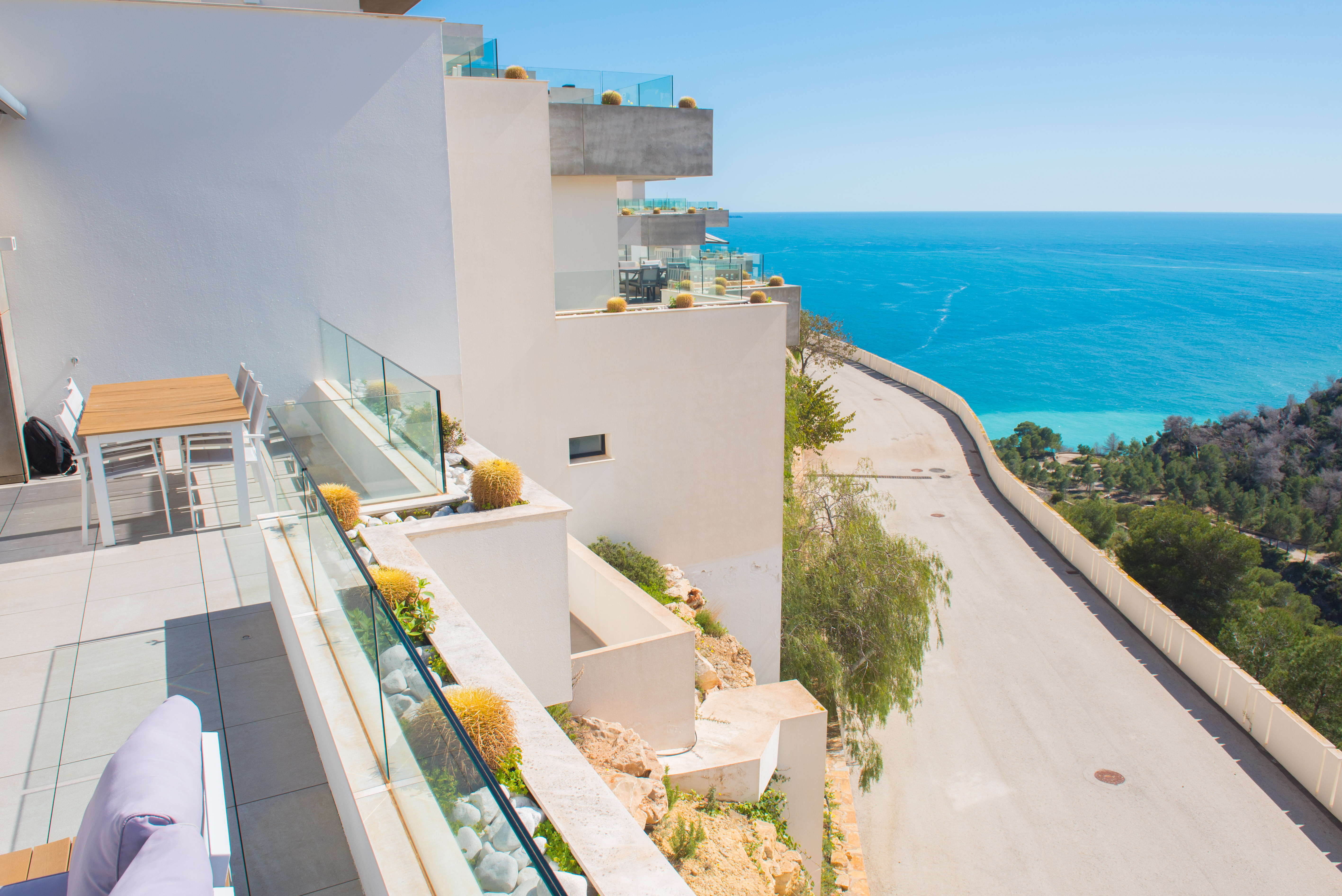 Private terrace featuring glass railings and integrated planters with cacti, overlooking the Mediterranean Sea and the rugged coastline of Benitachell.