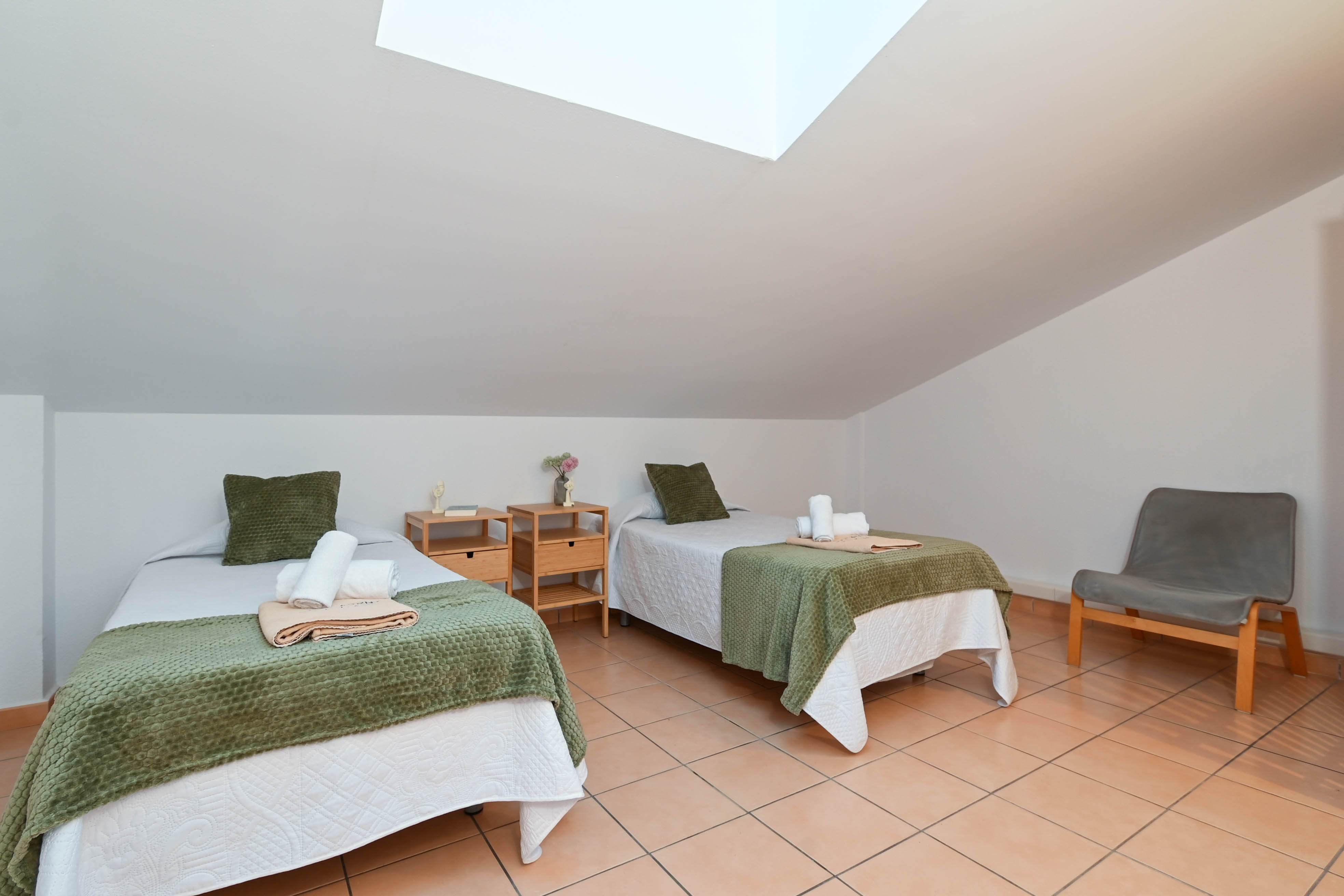 Attic bedroom featuring twin beds, terracotta tile flooring, and a skylight integrated into the sloped ceiling for natural illumination.